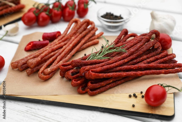 Fototapeta Delicious kabanosy with rosemary, peppercorn, chilli and tomatoes on white wooden table, closeup