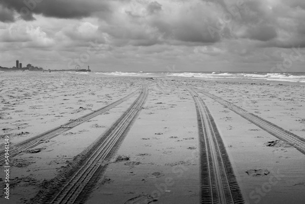 Obraz Tire tracks in the sand of a beach along the sea with a fierce sky and a Ferris wheel in the distance.