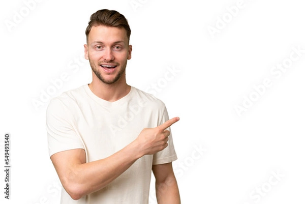 Fototapeta Young blonde caucasian man over isolated background surprised and pointing side