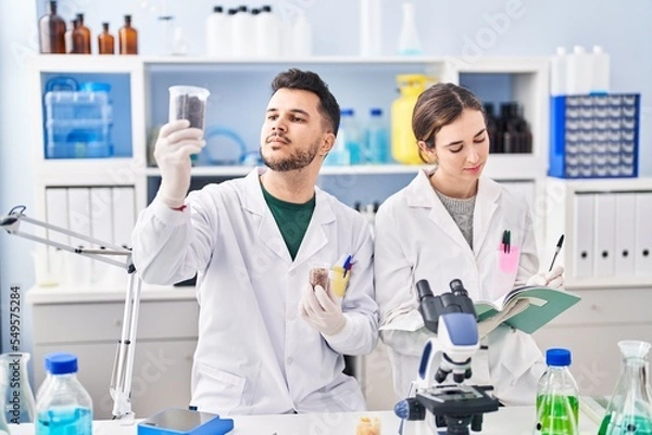 Fototapeta Man and woman wearing scientist uniform working at laboratory