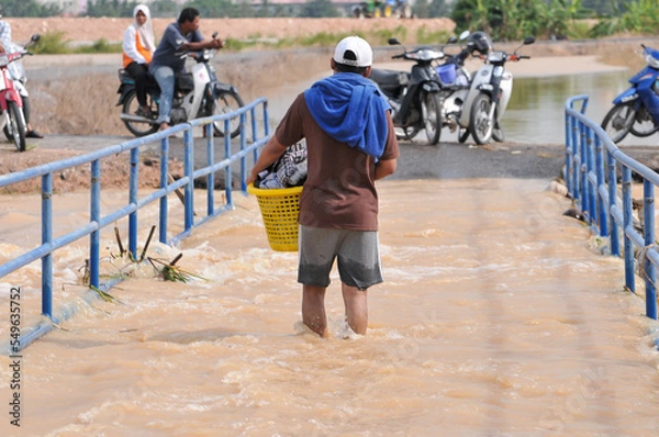 Fototapeta a man wading through the flood carrying a basket of clothes