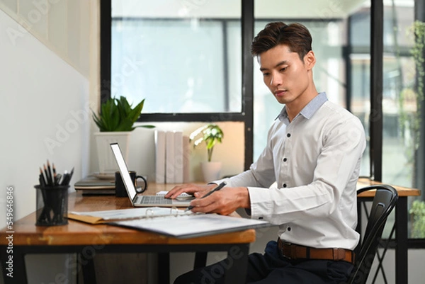 Fototapeta Focused handsome male entrepreneur using laptop, managing his small business from home