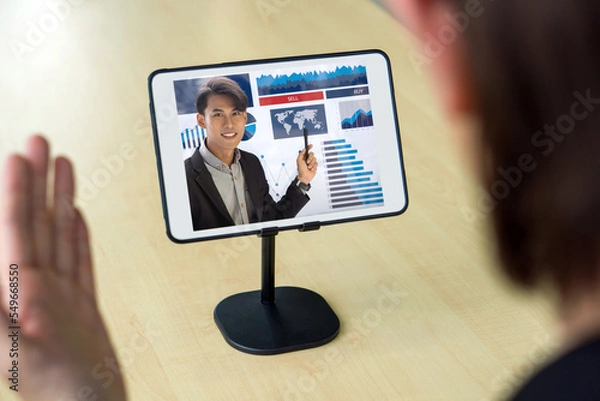 Fototapeta Back view of businessman in black suit have webcam conference through tablet computer with the investment advisor. Work from home concept