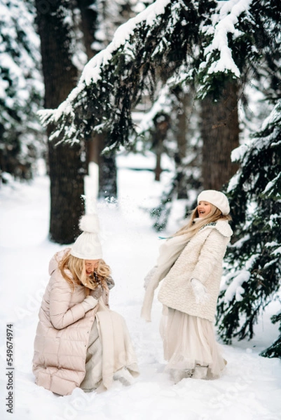 Fototapeta Handsome mother and daughter are having fun outdoor in winter time. Playing with snow in forest between snowy trees