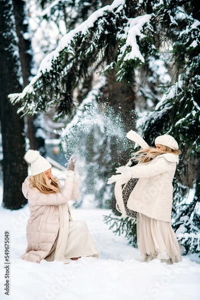 Fototapeta Handsome mother and daughter are having fun outdoor in winter time. Playing with snow in forest between snowy trees