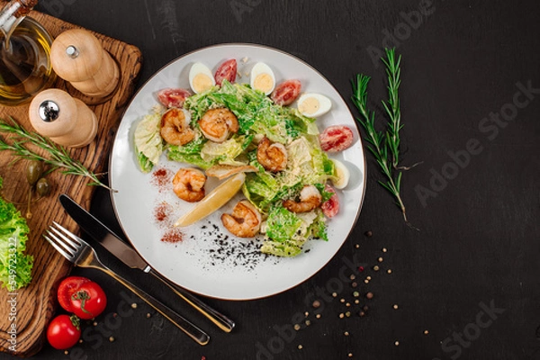 Obraz Tasty salad with shrimps, herbs and vegetables on black background