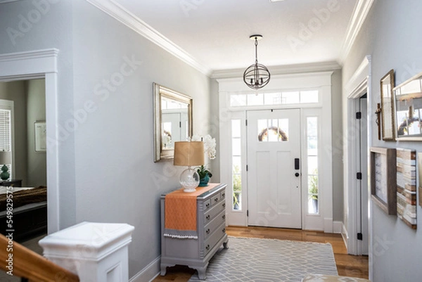 Fototapeta An open large and wide interior front door hallway foyer with transom, hanging light fixture, coastal colors and entry way table and wood floors