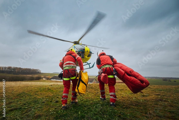 Fototapeta Two paramedic with safety harness and climbing equipment running to helicopter emergency medical service. Themes rescue, help and hope. ..