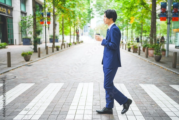 Fototapeta コーヒーを片手にオフィス街を歩くビジネスマン