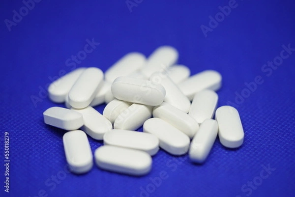 Fototapeta Heap of medical white pills on a blue background