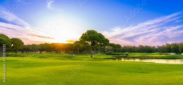 Fototapeta Panorama of dawn over the grass of a golf course with a lone tree in the foreground Belek Turkey