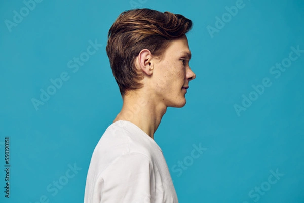 Fototapeta a man in a white T-shirt stands sideways to the camera on a blue background