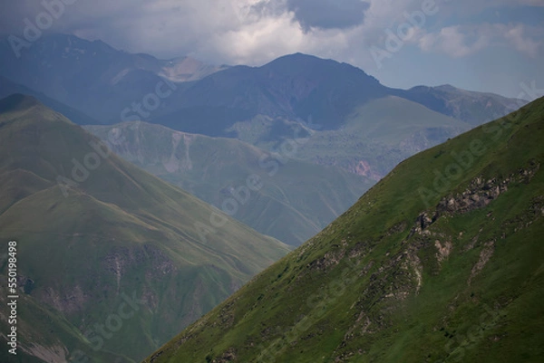 Fototapeta Mountains in clouds and clouds. Aerial view of a mountain peak with green trees in the fog. Beautiful landscape with high cliffs, forest, sky. mountain valley