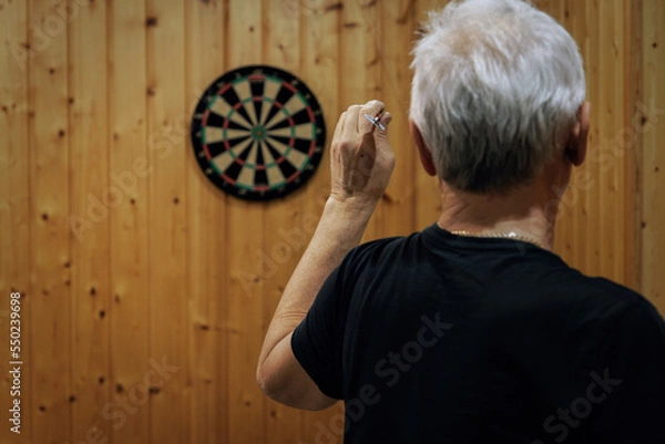 Obraz A man with gray hair plays darts. Rear View Of Man Playing Darts.