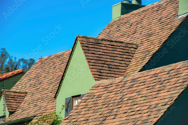 Fototapeta Waves of dark brown roofs with single gable style roof with green stucco exterior and visible shade on side of house or home