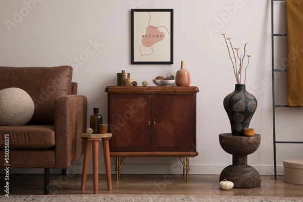 Fototapeta Interior design of cozy living room interior with mock up poster frame, brown sofa, stylish sideboard, vase with dried flowers, glass bottle, bowl with coconut, plaid, round pillows.  Home decor.