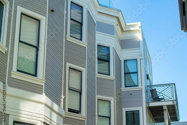 Obraz Building facade with wooden pannels and white accent paint around visible winows with clear blue sky background in late day shade
