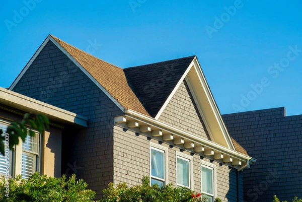 Fototapeta Double gable house with brown stucco with white window accent paint and visible blue windows and clear blue sky