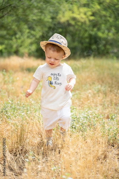 Fototapeta A kid in a straw hat runs across the field in summer