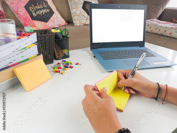 Obraz mockup image, Laptop computer with blank screen with a woman taking notes on yellow paper with pen in modern home room. mockups laptop