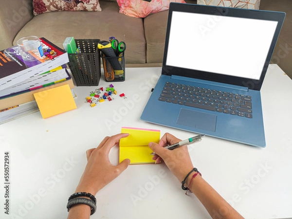 Obraz mockup image, Laptop computer with blank screen with a woman taking notes on yellow paper with pen in modern home room. mockups laptop