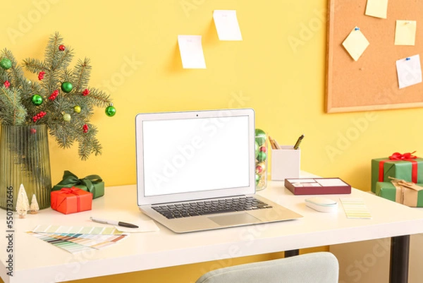 Fototapeta Workplace with laptop, fir branches in vase and Christmas presents near yellow wall
