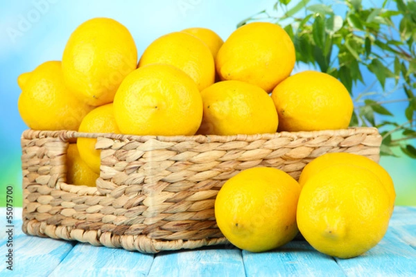 Fototapeta Ripe lemons in wicker basket on table on bright background