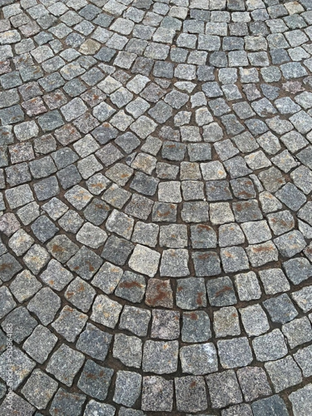 Fototapeta Stone old road, paving stones, closeup. Texture. Fragment of an ancient cobblestone alley. An example of paving from the past. Block paving. In the old days. Historical footprints