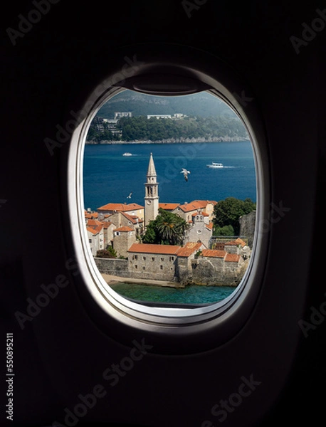 Fototapeta Old town of Budva, top view from porthole window of airplane, Montenegro. Concept for travel company or airway transportation.