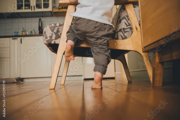 Fototapeta Bare heels of a toddler standing next to an armchair on a wooden floor at home