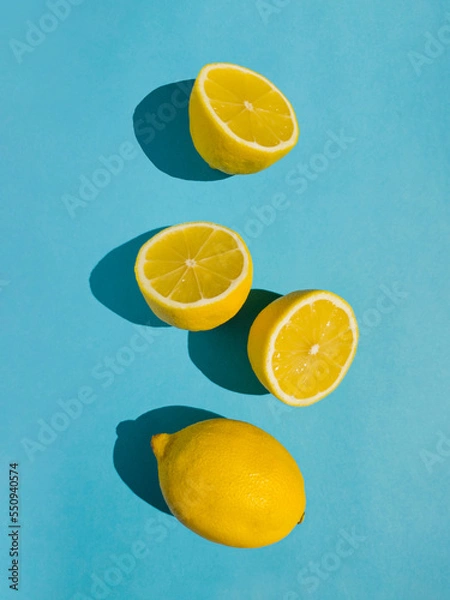 Fototapeta Juicy whole and half lemon and slices on bright pastel blue background. Minimal top view summer concept.