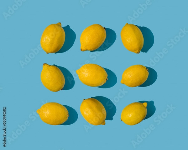 Fototapeta Summer frame pattern made with fresh yellow lemons on bright pastel blue background. Minimal concept on bright sunlight with sharp shadows.