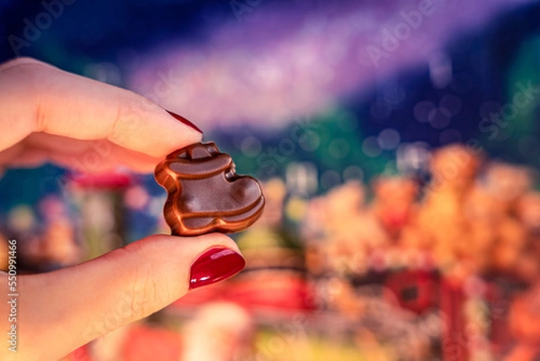 Obraz Christmas advent calendar chocolate for kids, girl holding a winter boot choco dessert, colorful blue, purple and orange bokeh bg