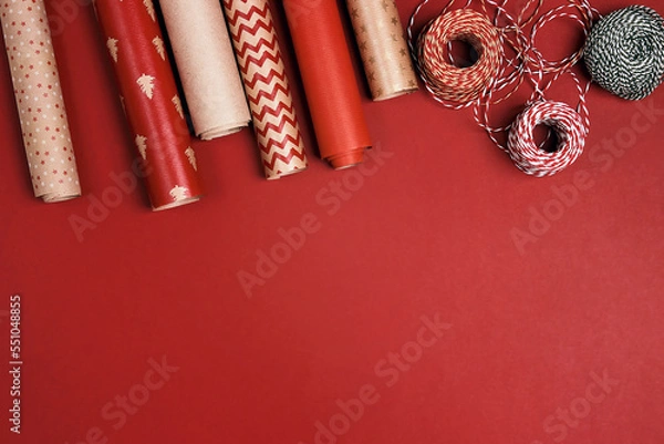 Obraz Christmas preparations with paper roll and decorative ropes on red background.