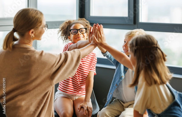 Fototapeta School psychologist with a group of  children conducts a mental health lesson and successful completion of collective school work