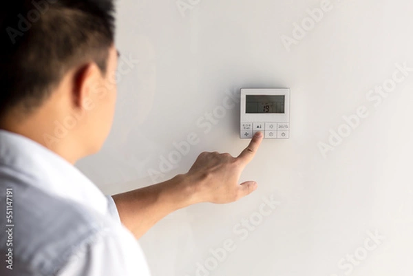 Fototapeta Close-up photo. The finger of a man's hand in a white shirt includes the buttons of the control panel of the air conditioner on the wall of the house, office.