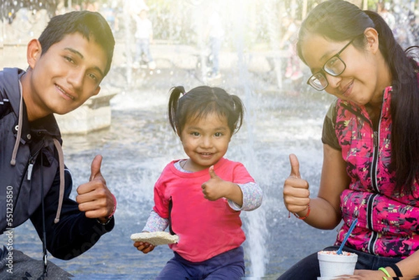 Fototapeta mexican family in park looking at the camera and making the sign of like with their hands