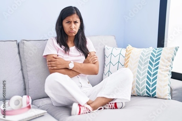 Obraz Young hispanic woman sitting on the sofa at home skeptic and nervous, disapproving expression on face with crossed arms. negative person.
