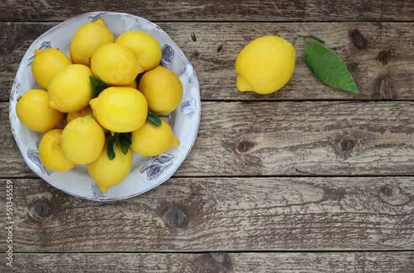 Obraz Fresh lemons fruit on plate on wooden table. Top view. Decorative arrangement of lemons with leaves on wood background.