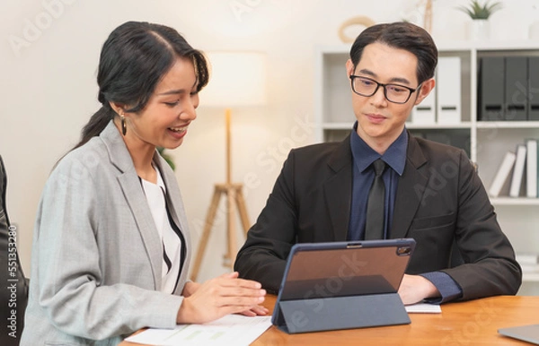 Fototapeta Smiling asian businesswoman showing tablet to her manager during a meeting in the office. secretary and boss in the office discuss new strategies and business development plans.