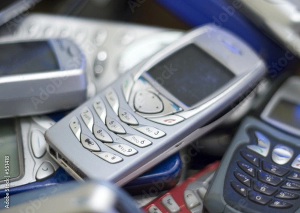 Fototapeta close up of silver cell phone on pile of others.