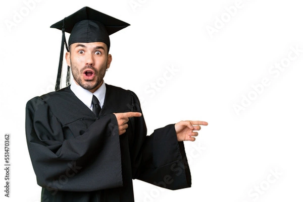 Fototapeta Young university graduate man over isolated chroma key background surprised and pointing side