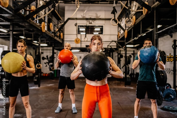 Fototapeta Sporty people in sportswear using exercise ball while having workout at industrial gym..Group training, teamwork concept. Horizontal shot. Front view