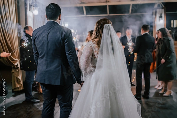 Fototapeta A crowd of young happy people with sparklers in their hands during celebration. Sparkler in hands on a wedding - bride, groom and guests holding lights in hand. Sparkling lights of bengal fires. 2023