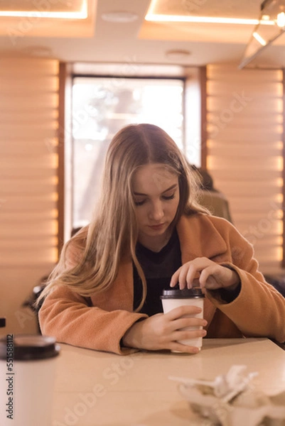 Obraz beautiful young woman with a glass of takeaway coffee sits in a cafe