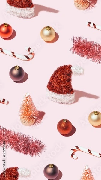 Fototapeta Trendy vertical Christmas wallpaper with red New Year's decorations on pastel pink background. Xmas pattern made of shiny props.