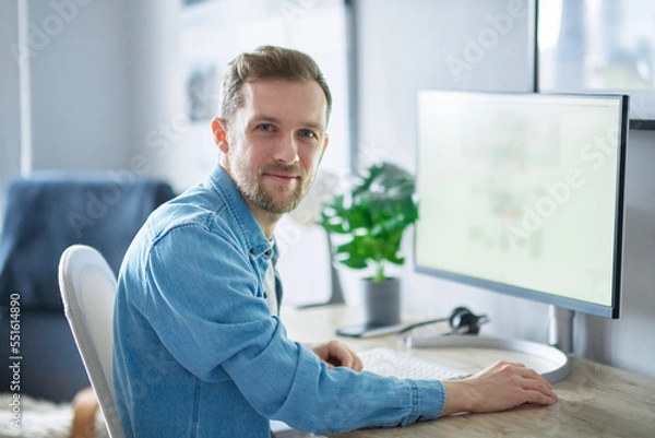 Obraz Young handsome IT support man in denim shirt . Attractive bearded caucasian male freelance software engineer sitting at working place in office hardly working using computer. High quality image