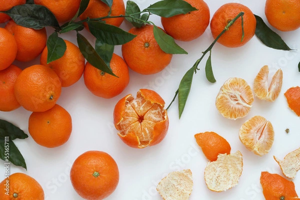 Obraz Tangerine and clementine citrus fruits with leaves on white background. Group of arranged mandarins and clementines with leaves, peeled fruit and scattered peel. Top view.