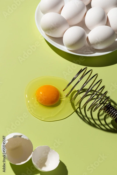 Fototapeta Raw egg yolk broken on a green background, next to the shell and a plate of eggs