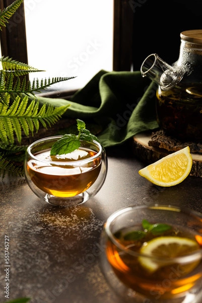 Fototapeta A glass mug with tea in the light is on the table. Custard tea with lemon